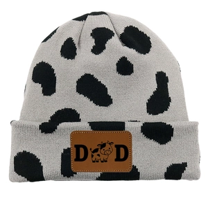 Detail of knitted cow print beanie featuring a brown leather patch with DAD text