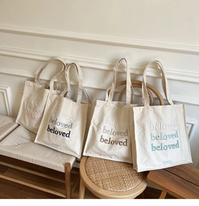 Detail showing four embroidered canvas tote bags in pink, blue, and brown on wooden stools