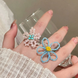 Bagues artisanales en perles avec fleurs roses et bleues portées à la main