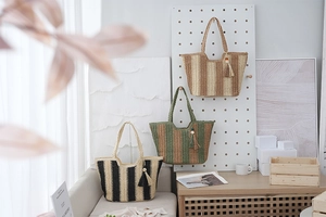Detailed view of three striped straw tote bags with matching tassels on a wooden shelf