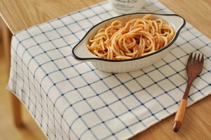 Blue plaid cotton placemat with white ceramic bowl and wooden fork on a warm wooden table