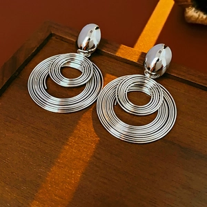 Detail of silver coiled spiral hoop earrings on a vintage wooden tray with soft lighting