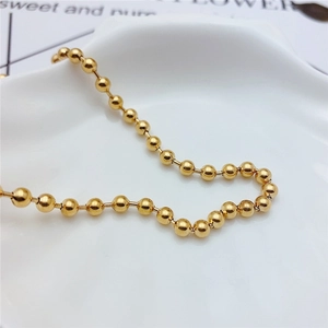 Macro detail of a minimalist gold bead choker chain displayed on a white ceramic tray