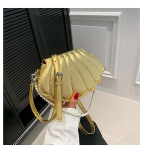Detail of gold shell-shaped crossbody bag with pearl chain handle and metallic finish