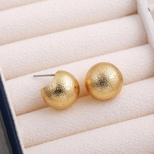 Close-up of golden matte hollow ball stud earrings in a white textured jewelry box