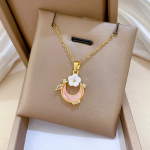 Detailed shot of a gold crescent moon necklace with pink inlay and white floral accents