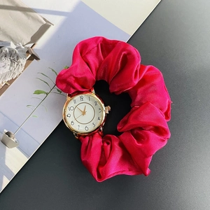 Detail view of red silk scrunchie watch band with gold case on a stylish dark surface