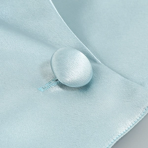 Détail macro du tissu satiné bleu clair avec bouton recouvert assorti sur le vêtement