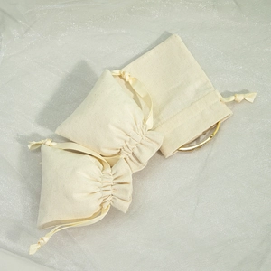 Three beige cotton drawstring jewelry pouches in various sizes with a gold bracelet