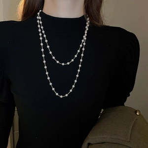 Gros plan d'un collier de perles double couche sur un pull noir, style vintage