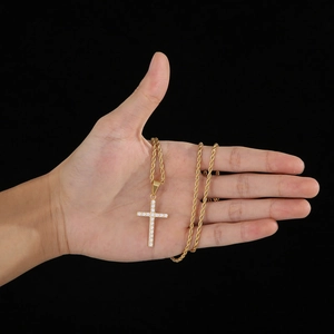 Gros plan détaillé du pendentif croix dorée avec cristaux tenu dans une main