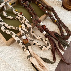 Detail of hand-woven cotton linen belt with resin beads and amber accents on wooden tray