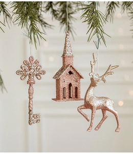 Macro shot of rose gold glitter Christmas ornaments featuring elk and house hanging on pine