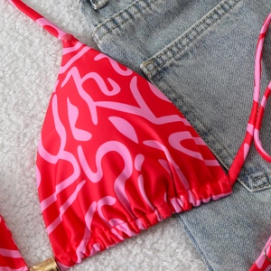 Detail of red bikini top with pink abstract patterns and gold metal ring decorative accents