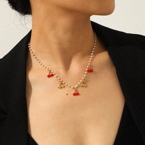 Gros plan du collier pendentif cerise avec perles blanches porté sur le cou d'un mannequin