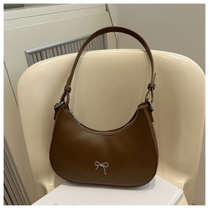 Close-up of a brown crescent shoulder bag with a silver bow on a cream chair