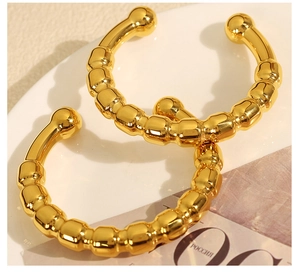 Close-up detail of golden metal ear cuffs featuring unique raised spherical texture and C-shape