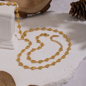 Close-up of golden heart chain necklace on white stone with decorative autumn props