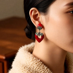 Close-up of a model wearing red strawberry heart earrings with vintage gold leaf detail