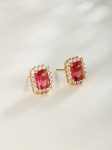 Close-up of golden geometric earrings featuring rectangular red gemstones and white crystals