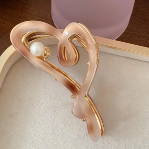 Detailed view of heart-shaped gradient pink hair claw with pearl accent on a beige tray