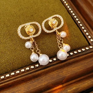 Detail of gold rose earrings with zircon frame and hanging pearls on velvet