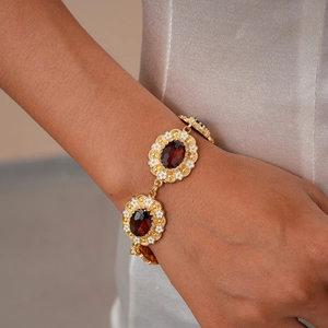 Detail of vintage gold bracelet with deep red gems and white floral enamel accents