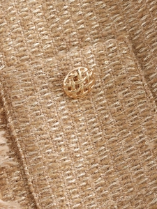 Detailansicht einer Tweed-Jacke mit strukturiertem Stoff und goldfarbenem Knopf