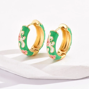 Close-up of gold-plated hoop earrings with green enamel and pink flower pattern