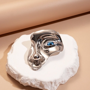 Broche visage argentée artistique avec détail œil bleu sur fond de pierre blanche