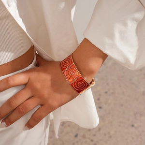 Close-up of vintage orange enamel cuff bracelet with golden spiral patterns on a wrist
