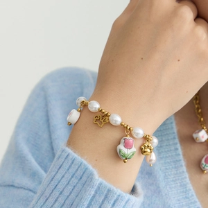 Elegant stainless steel bracelet with ceramic floral pendant and pearls on model wrist