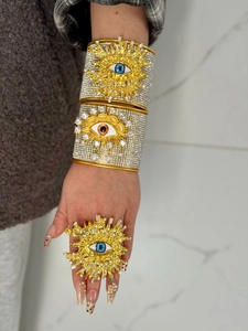 Brazaletes dorados de ojo turco y anillo de diamantes de imitación a juego en la mano