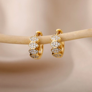 Macro shot of gold-plated marquise zircon C-shaped earrings on a natural wooden branch