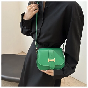 Detail of a bright green crossbody saddle bag with a prominent golden H-shaped buckle