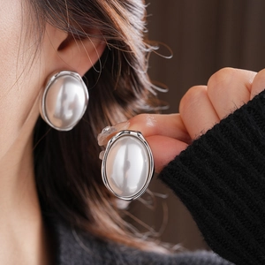 Detail of large oval pearl stud earring with silver textured frame on model