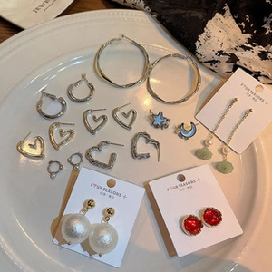 Assorted earring set with faux pearls, ruby-colored studs, and metal hoops in a ceramic dish