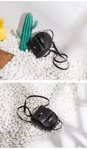 Detail eines schwarzen Mini-Rucksacks aus PU-Leder mit goldenem Logo auf Kieselsteinen