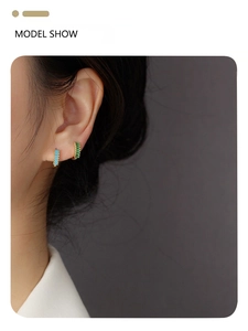 Close-up of golden hoop earrings with turquoise and green stones on a model