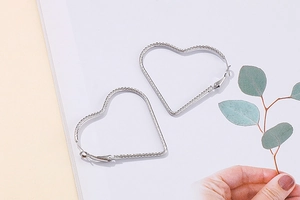 Detail of silver heart hoop earrings with spiral texture held against a soft background