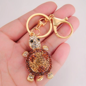Macro shot of gold turtle keychain with amber rhinestones held in hand for scale