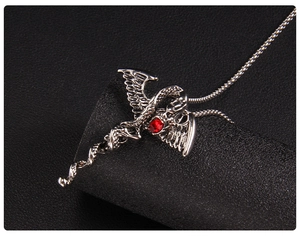 Gros plan d'un collier croix gothique en argent avec pierre rouge et ailes d'ange