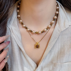 Detail of layered gold necklace featuring tiger eye stone pendant and warm pearl beads