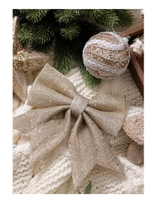 Golden glitter bow detail with festive ornaments on a soft white knitted texture