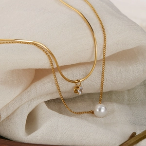 Elegant gold double-layer necklace with pearl and zircon charms on a textured background