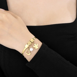 Detail view of gold snake chain bracelet with heart, pearl and angel silhouette charms