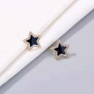 Macro shot of gold star earrings with black enamel center and white zircon stones