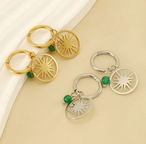 Detail of gold and silver sunburst hoop earrings with green bead accents on silk