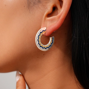 Macro side view of C-shaped enamel hoop earrings with blue and yellow wave patterns