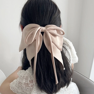 Macro shot of beige satin bow hair clip with pearl detail worn on the back of head